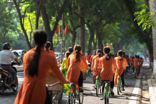 Grand voyage en Indochine de Hanoi: Hanoi Vietnamese girls wear traditional long dress Ao Dai cycling on street