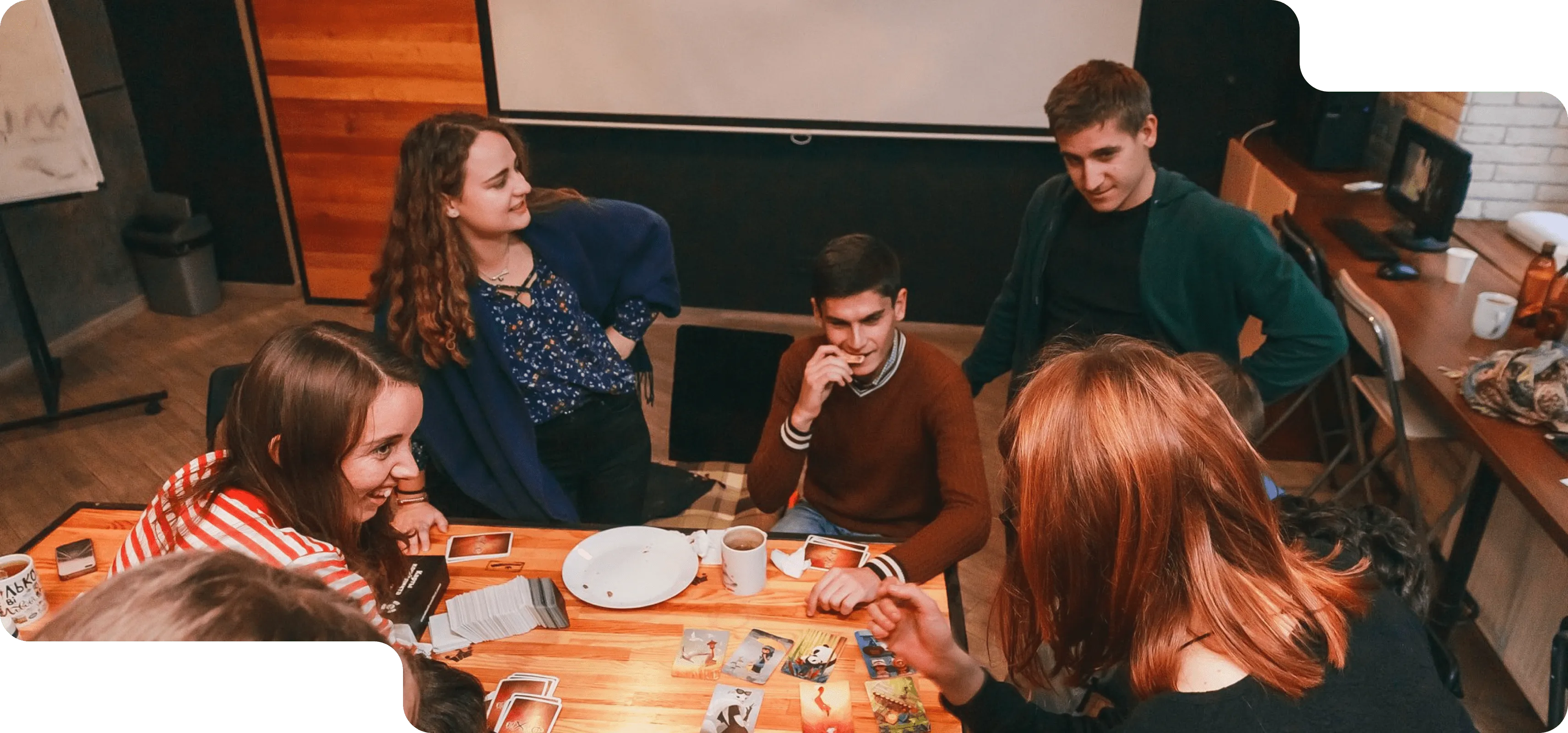 Молоді люди сидять за столом усміхаються, грають в карти