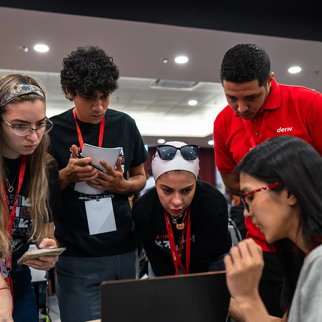 Deriv team members collaborating around a laptop at a company event, showcasing teamwork and innovation