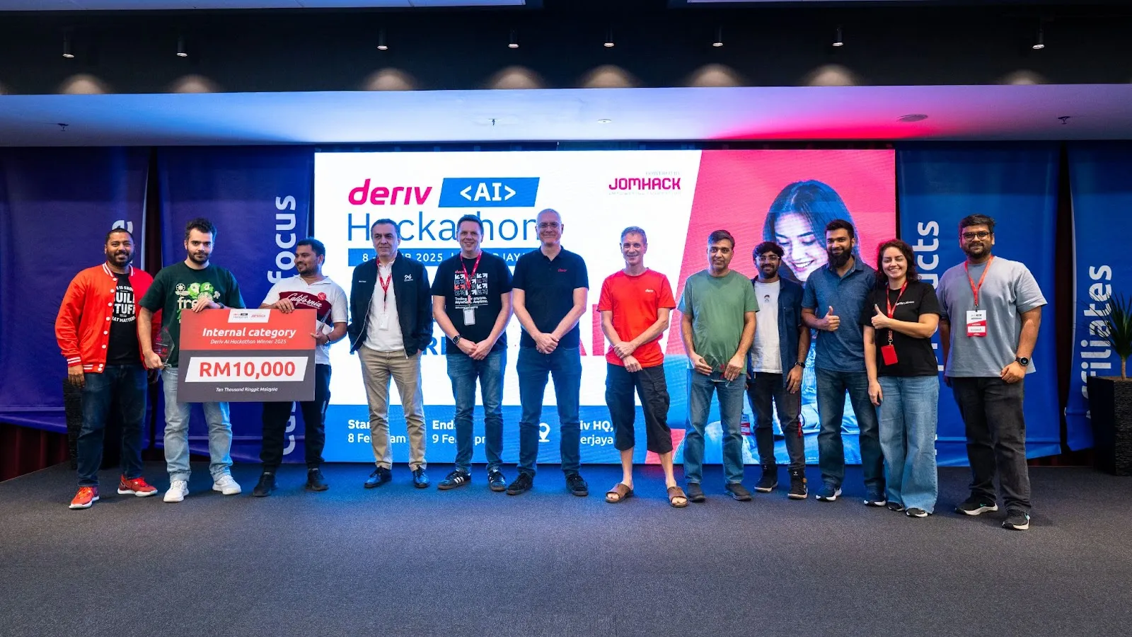 Internal innovation winners from the second AI Hackathon at Deriv standing on stage, holding a prize cheque, celebrating their achievement.