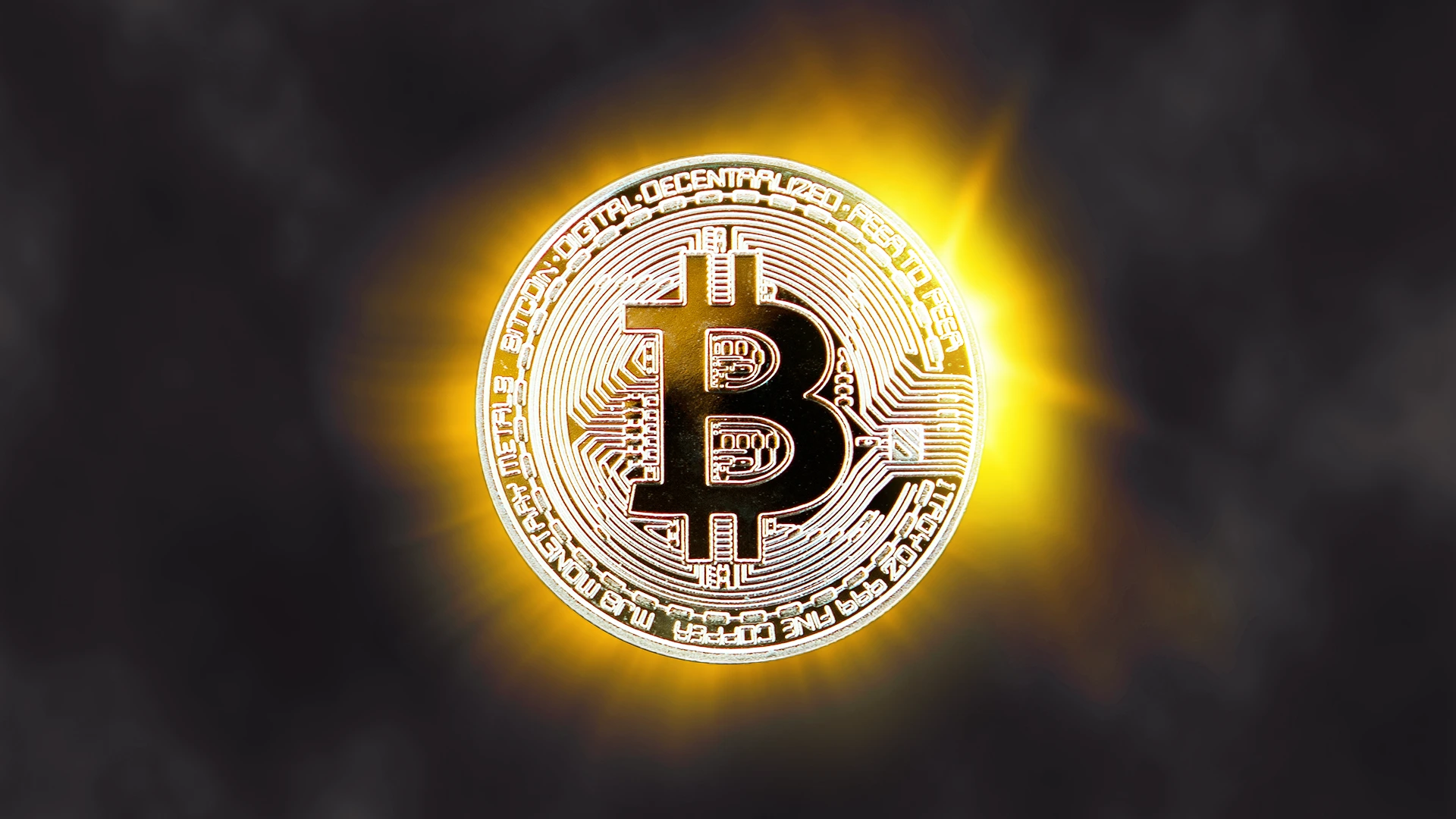 Illustration of a golden Bitcoin coin glowing with bright yellow light against a dark background.
