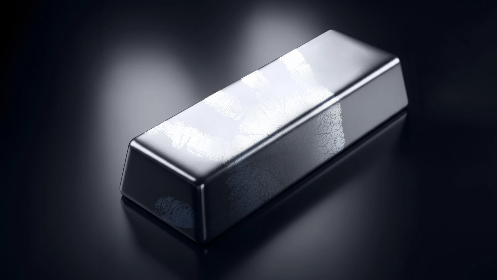 A close-up of a polished silver bar placed on a dark reflective surface. The bar has a smooth metallic sheen with visible scuff marks and fingerprints on its surface