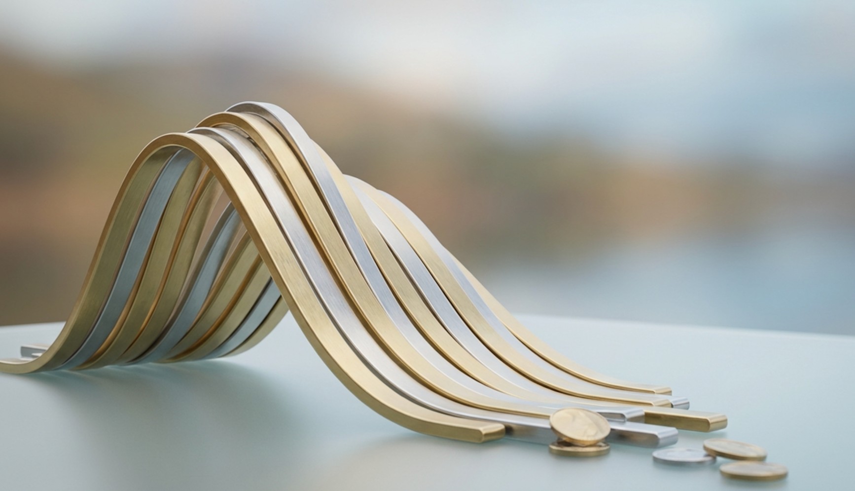 Curved gold and silver metal strips forming a wave shape on a table, with scattered coins in the foreground.