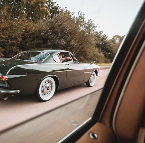  A man is driving a green car on a road.