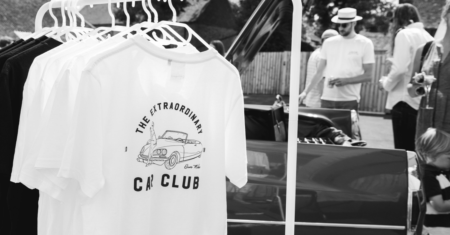  A white shirt with a car on it hangs on a rack.