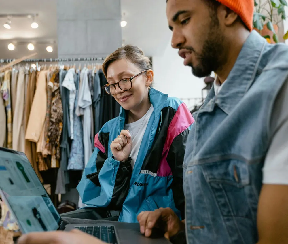 Lotus United team members collaborating in retail store environment with laptop, apparel displays, and casual workplace culture