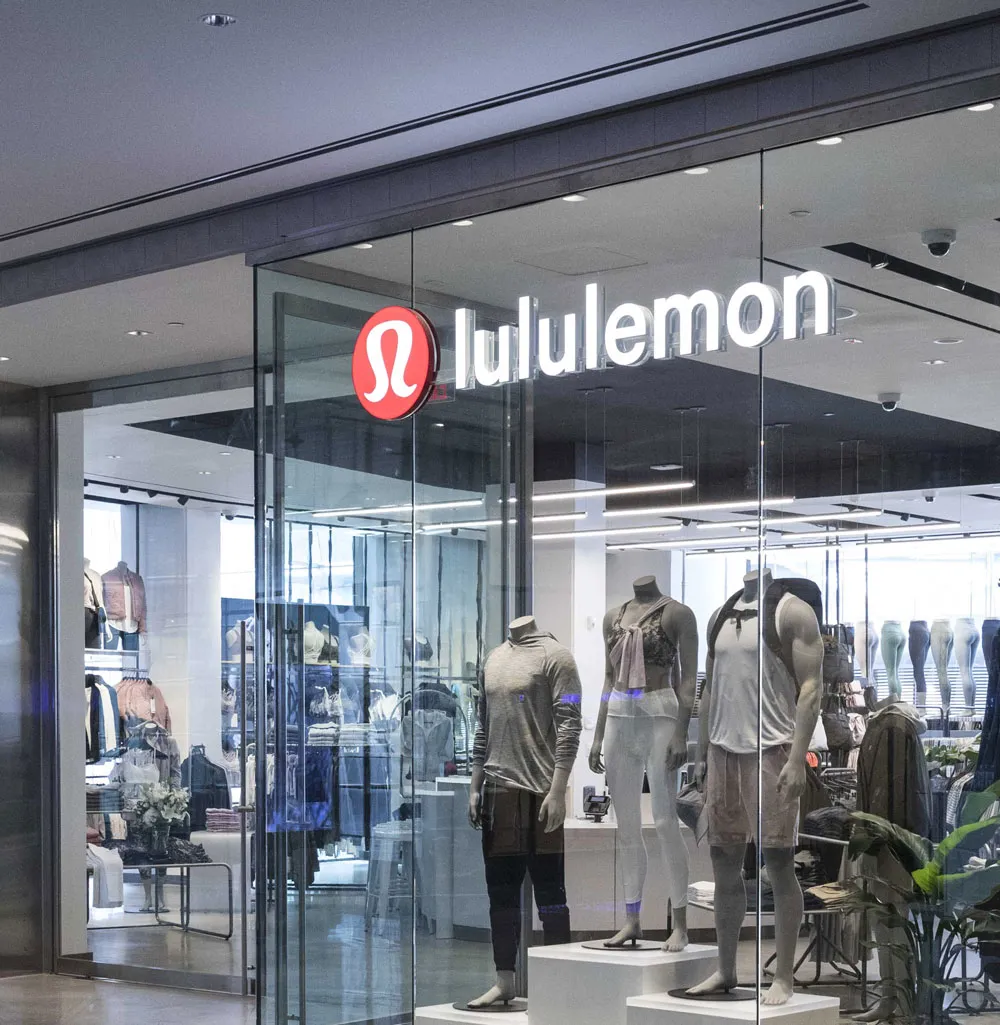 Lululemon retail storefront with glass doors, red circular logo, and apparel displays