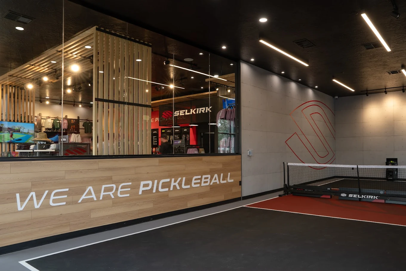 Selkirk pickleball retail store with wooden display fixtures, apparel merchandising, 'We Are Pickleball' branded signage, and integrated pickleball court