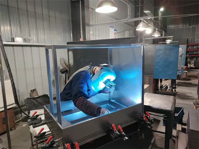Metal fabrication work in progress with welding arc visible on monitor screen in manufacturing facility