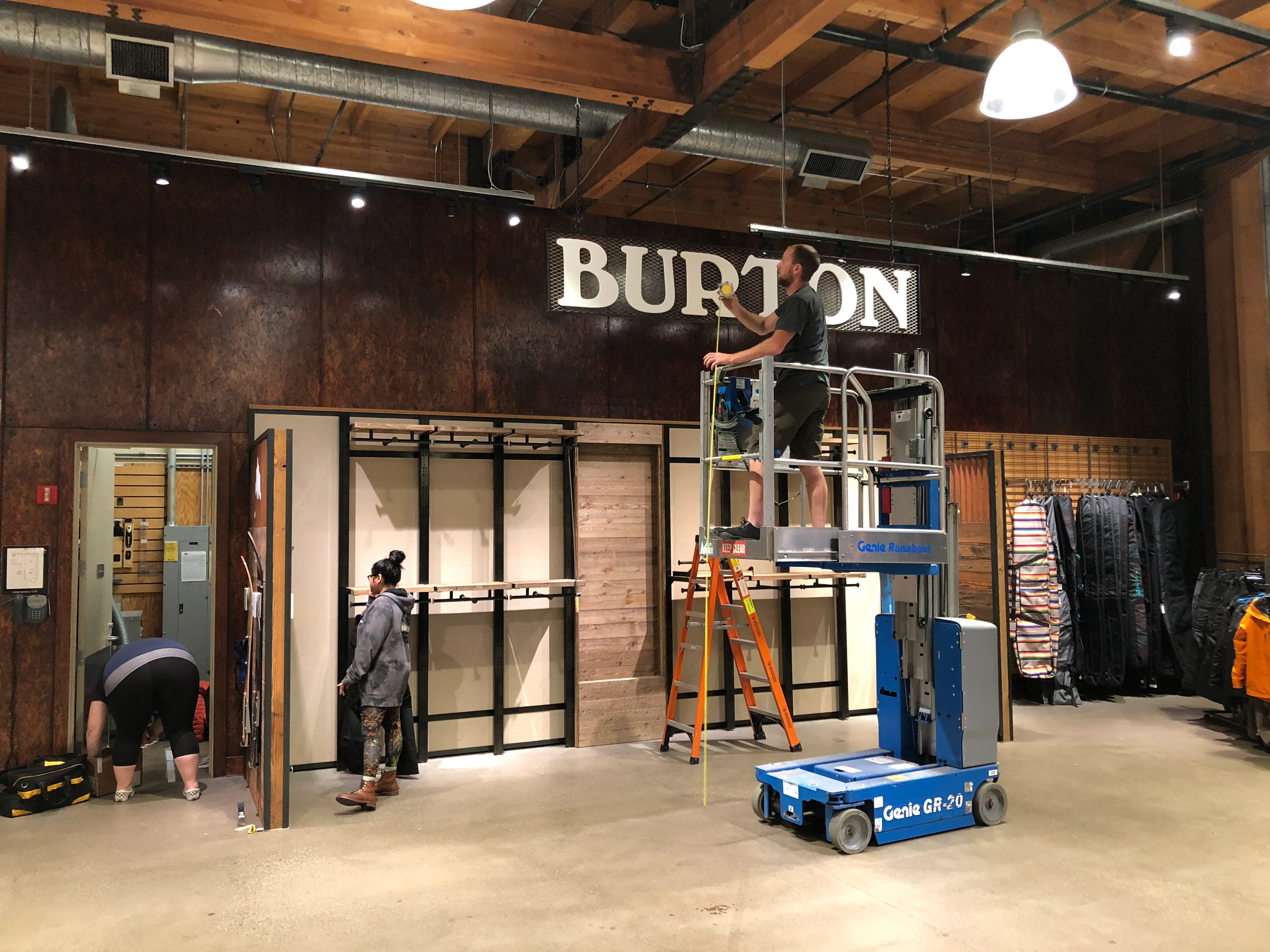 Burton retail installation at REI location with branded storefront signage, metal frame fixtures, and installation crew during buildout