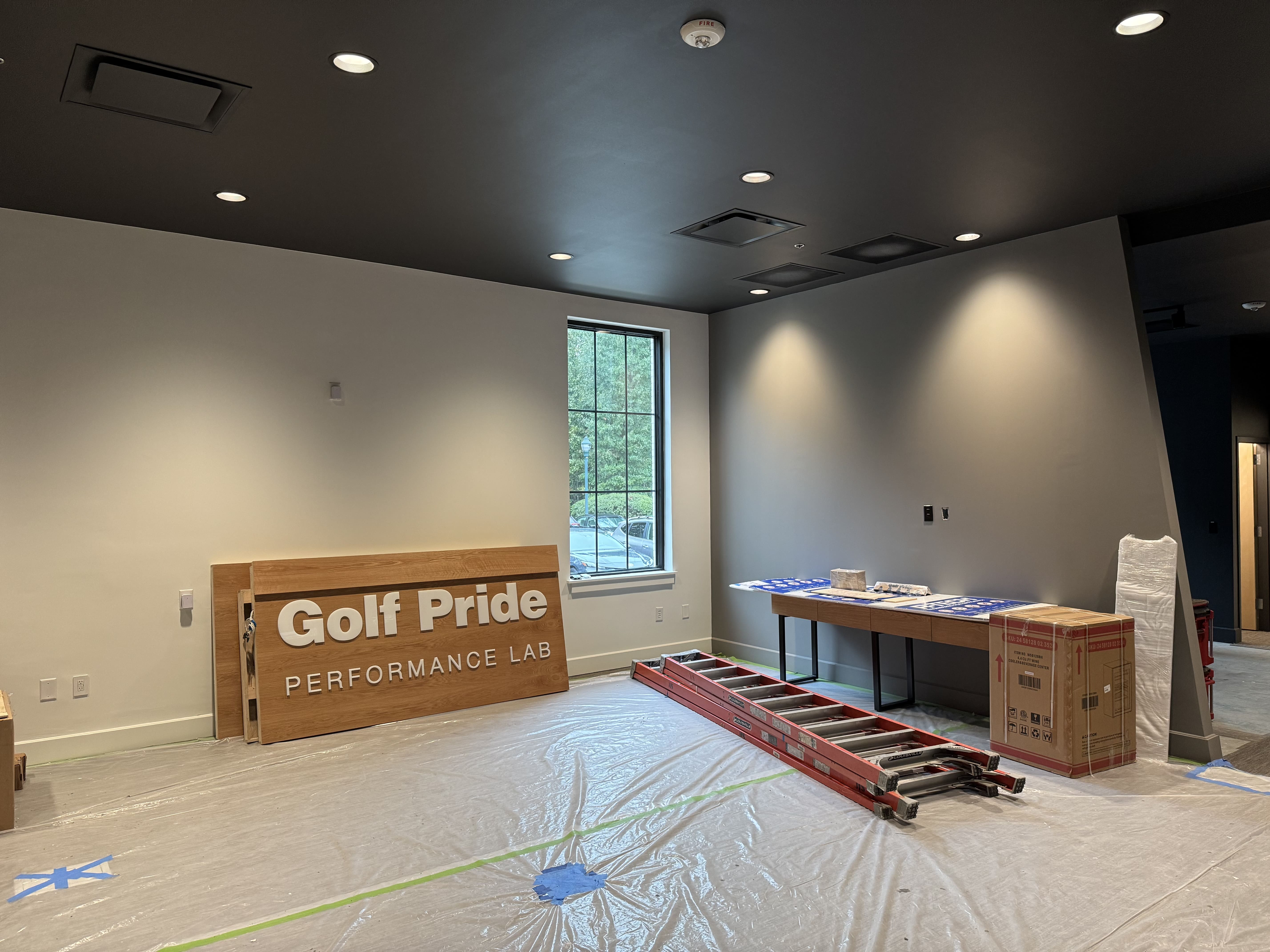 Golf Pride Performance Lab installation in progress with branded signage, wooden fixtures, flooring protection, and fitted equipment setup