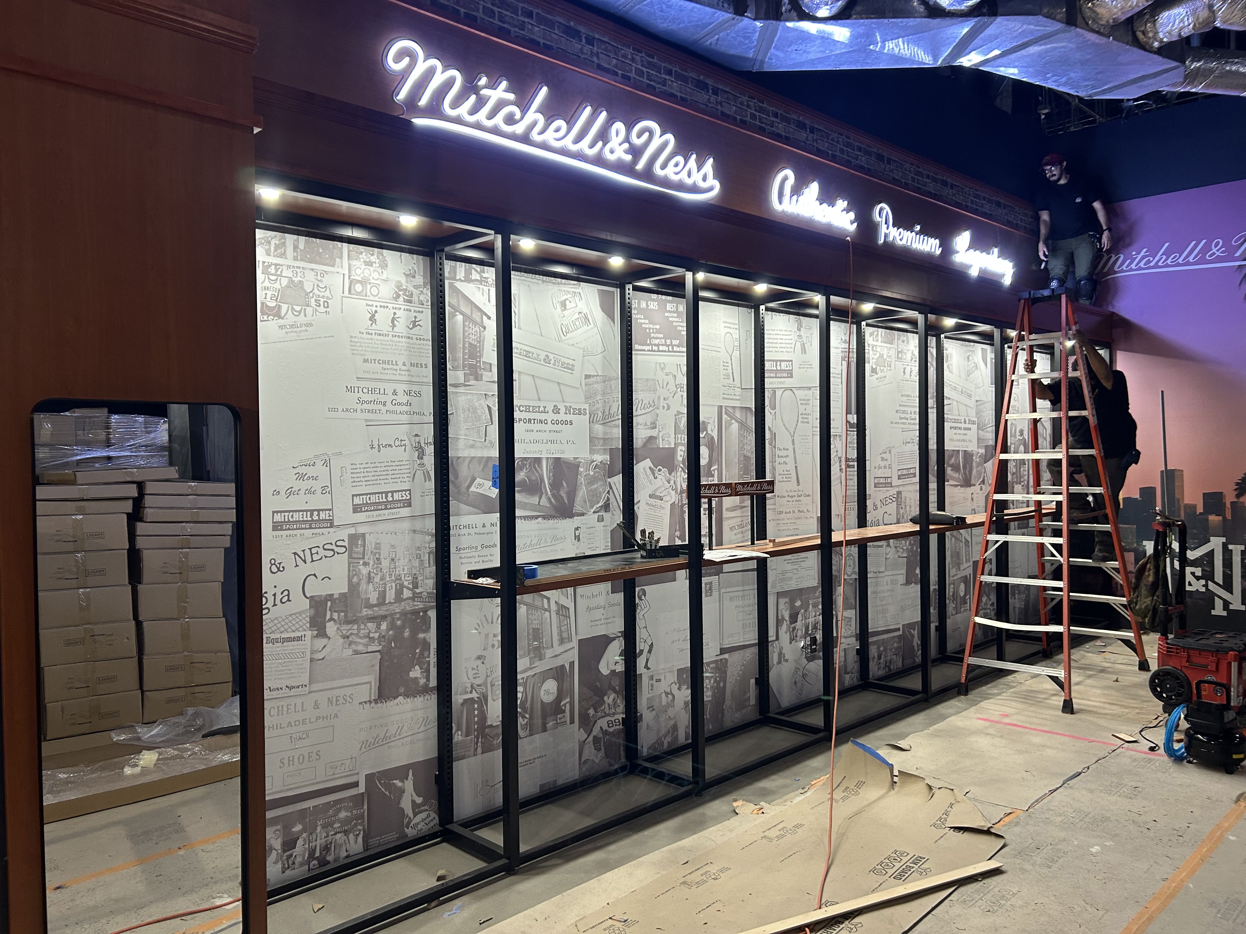 Mitchell & Ness storefront installation with neon signage, metal frame glass doors, and vintage basketball memorabilia displays