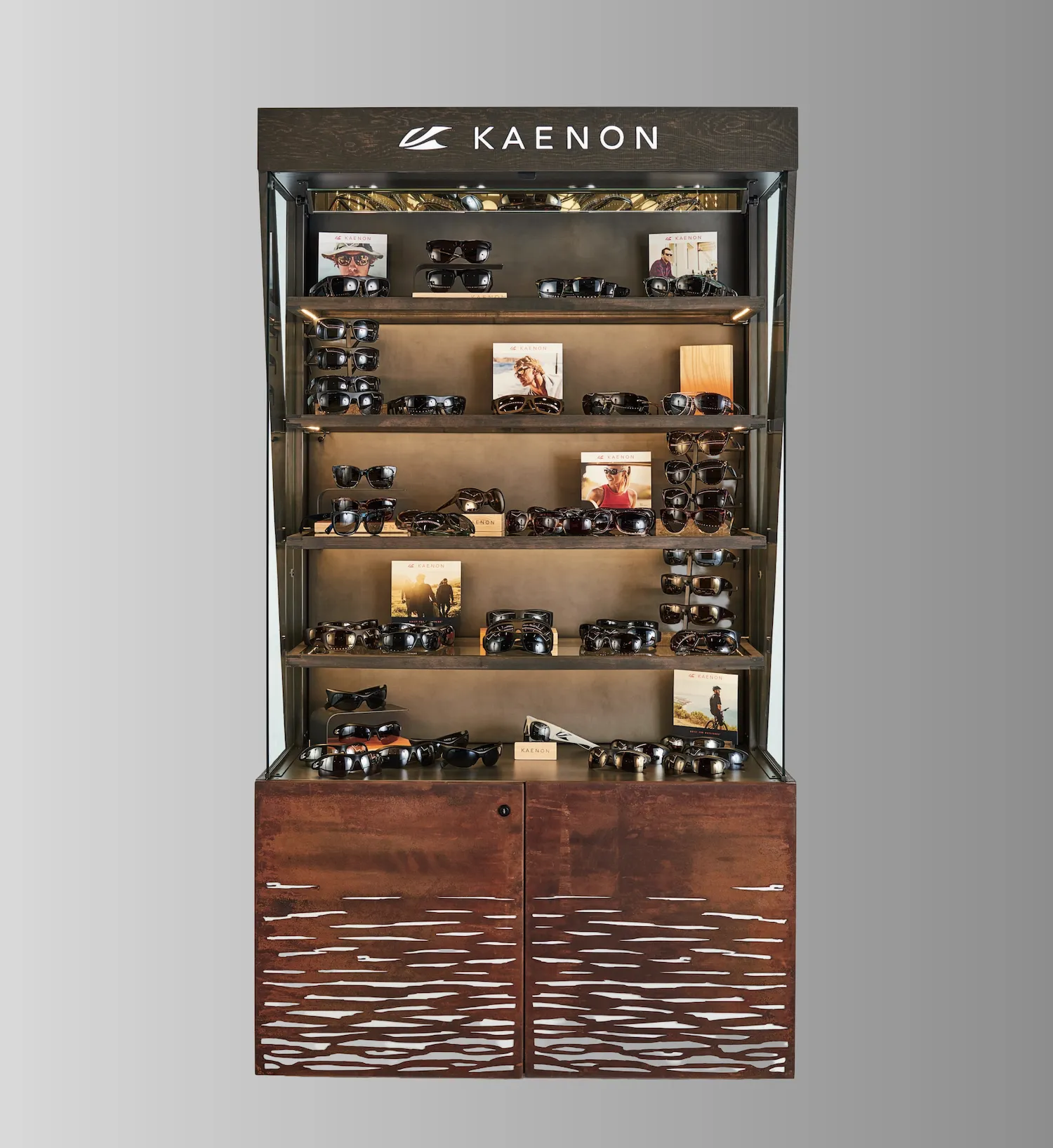 Kaenon eyewear retail display case with tiered shelving, illuminated backdrop, wood base with textured doors, and product photography displays