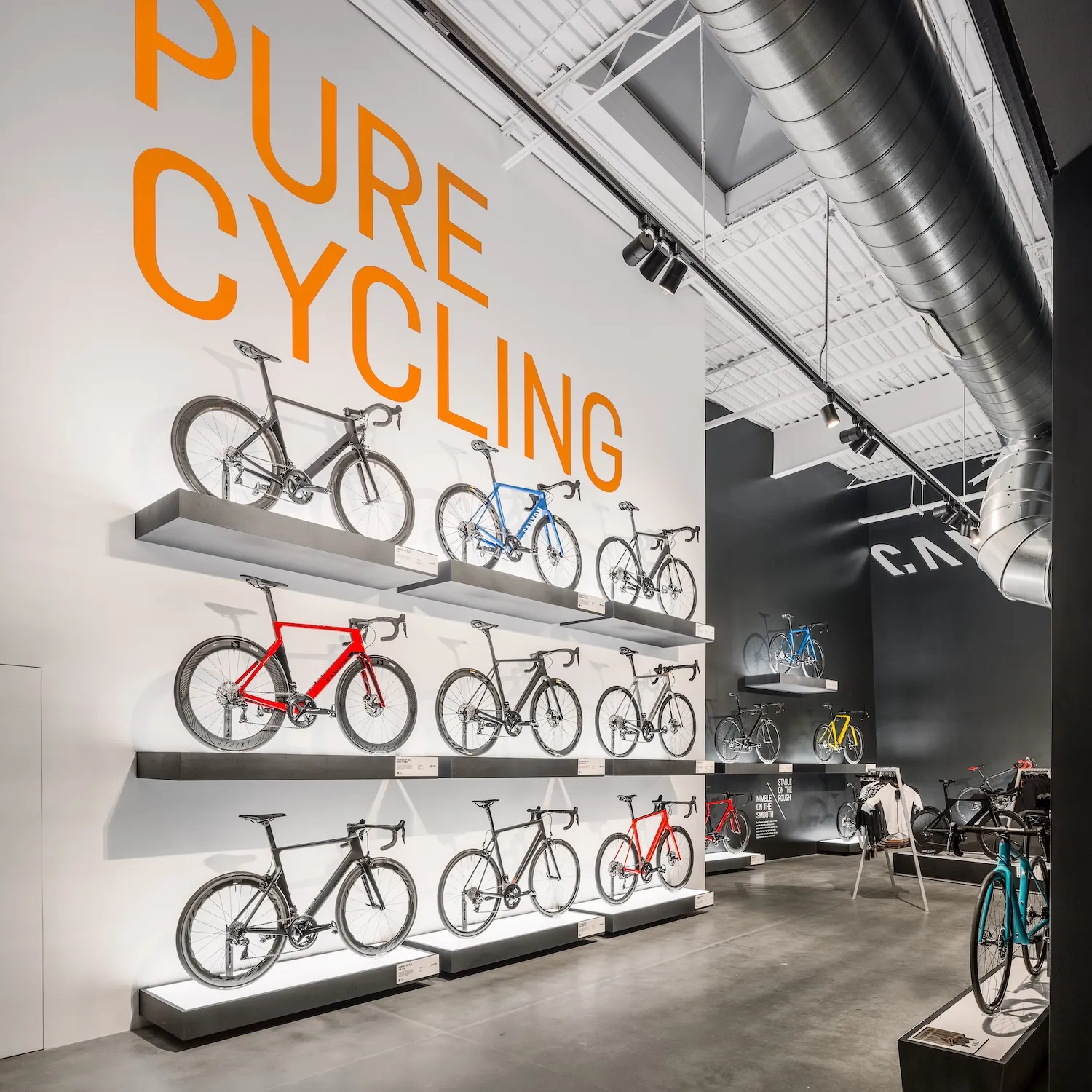 Canyon Carlsbad retail store featuring tiered white display shelving with multiple bicycles, orange and blue branding, and bike merchandise displays