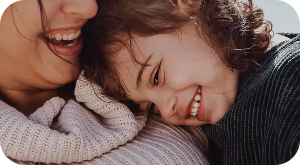 Close-up of a smiling child resting their head affectionately on an adult's chest, both wearing knitted sweaters.
