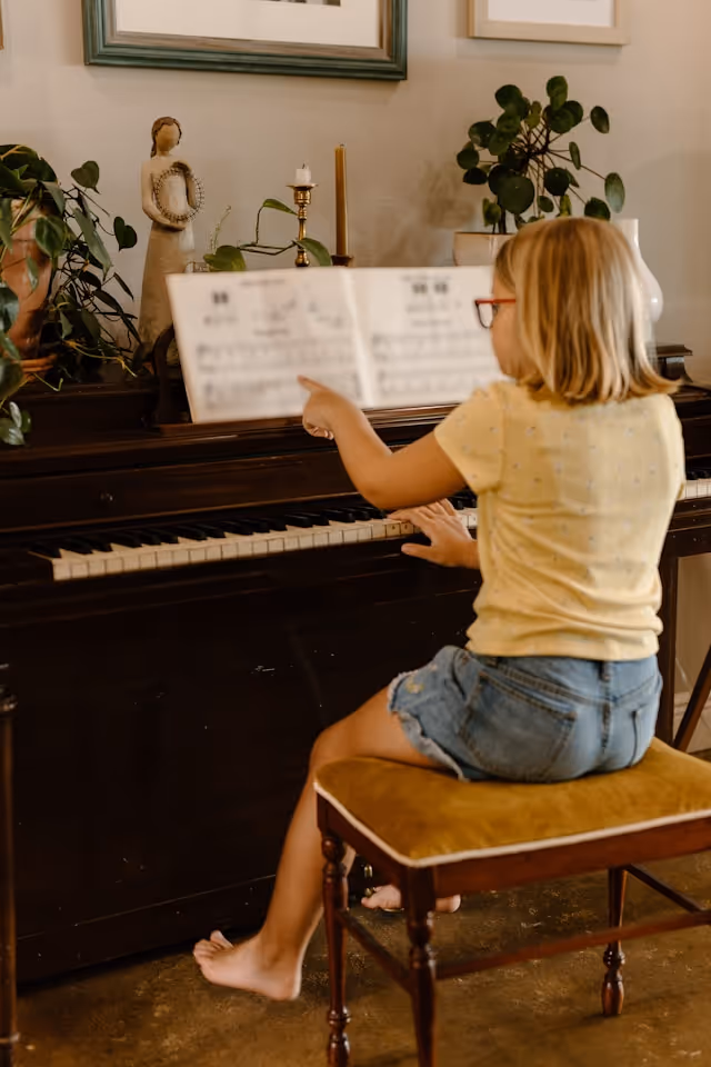 A girl struggling at the piano trying to read a traditional piano lesson book.