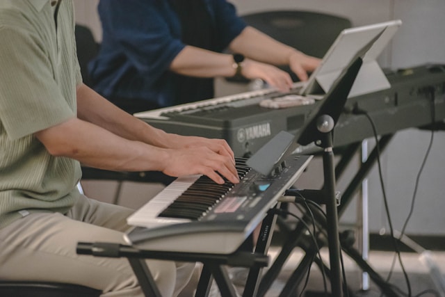 Persons practicing piano with a keyboard and laptop.