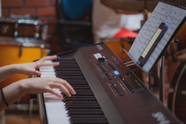 Person practicing piano with a smartphone and sheet music on a digital keyboard.