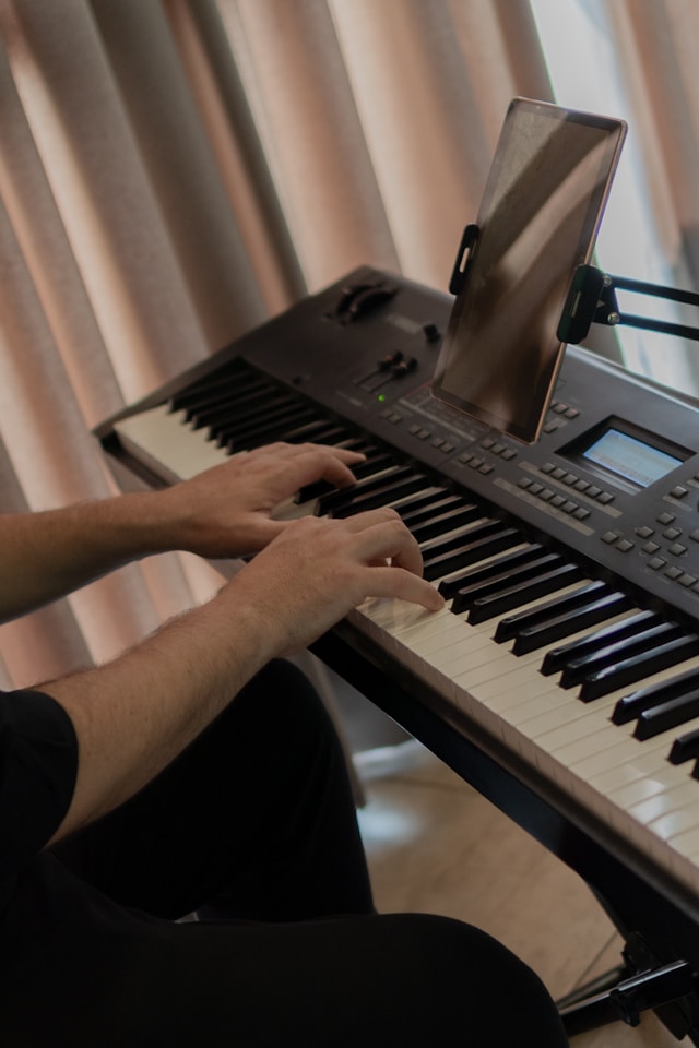 Adult practicing piano with a tablet beside a digital keyboard.