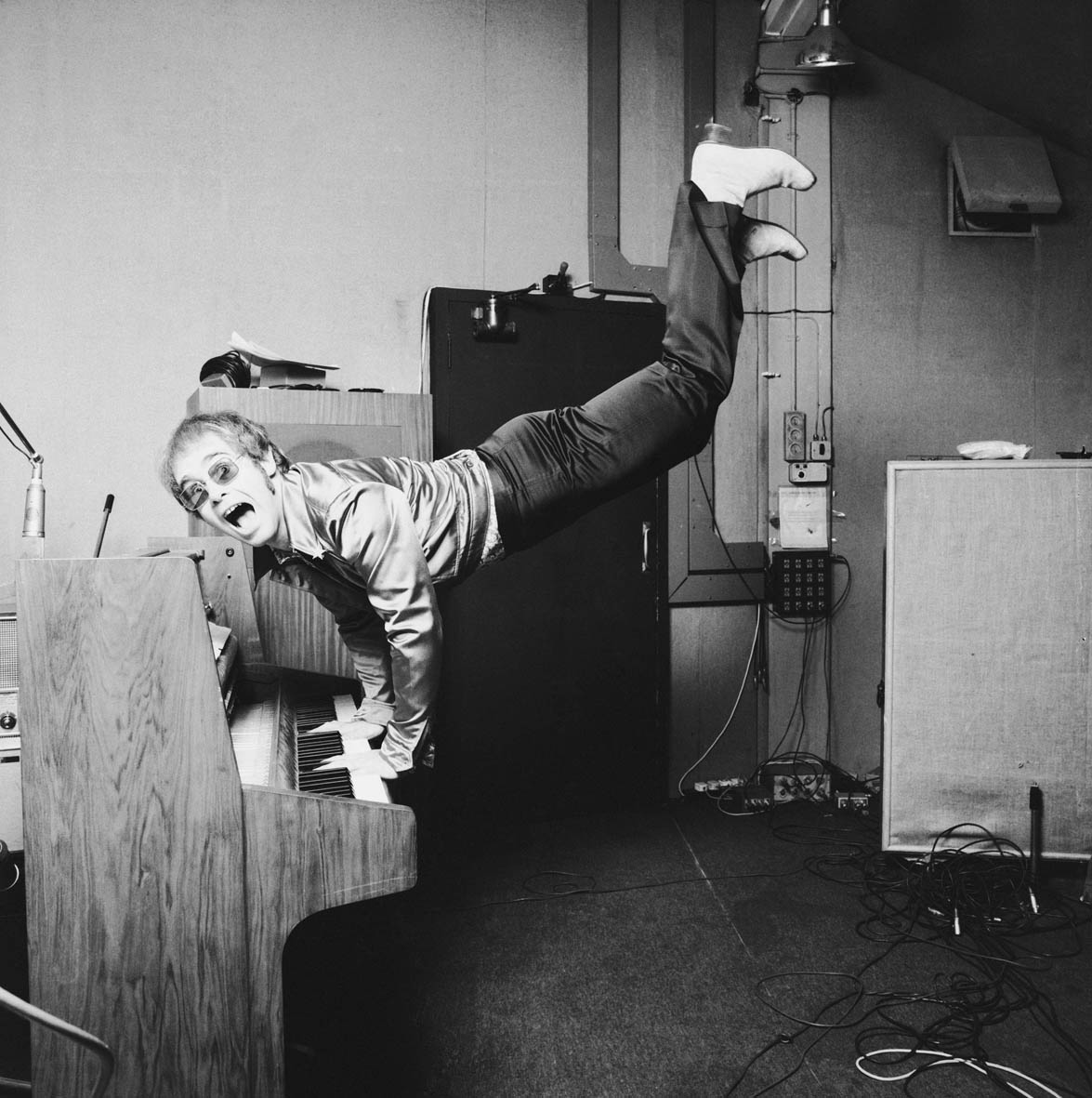 Elton John being wild with his legs and feet in the air dancing at the piano.
