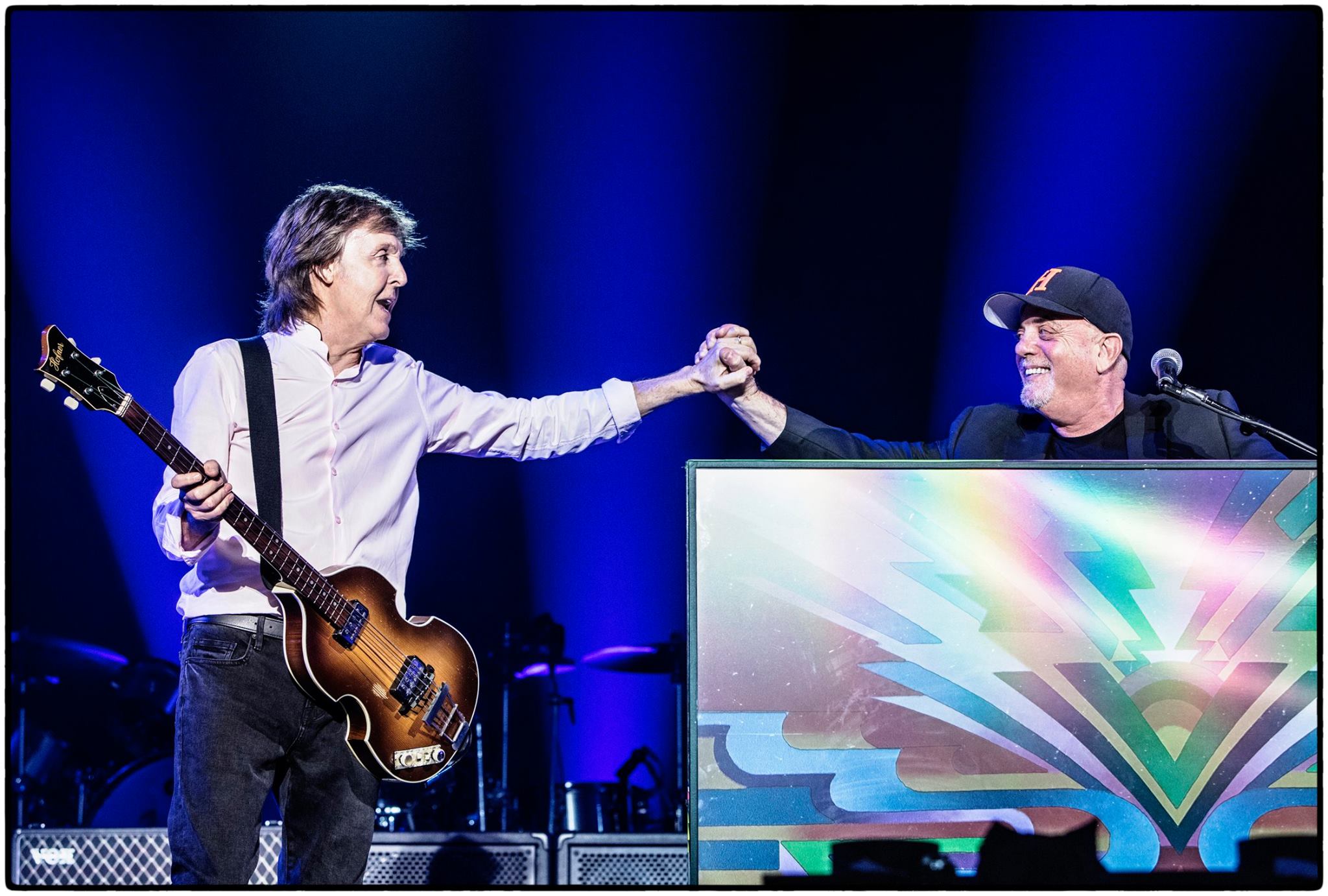 Paul McCartney and Billy Joel on stage holding hands.