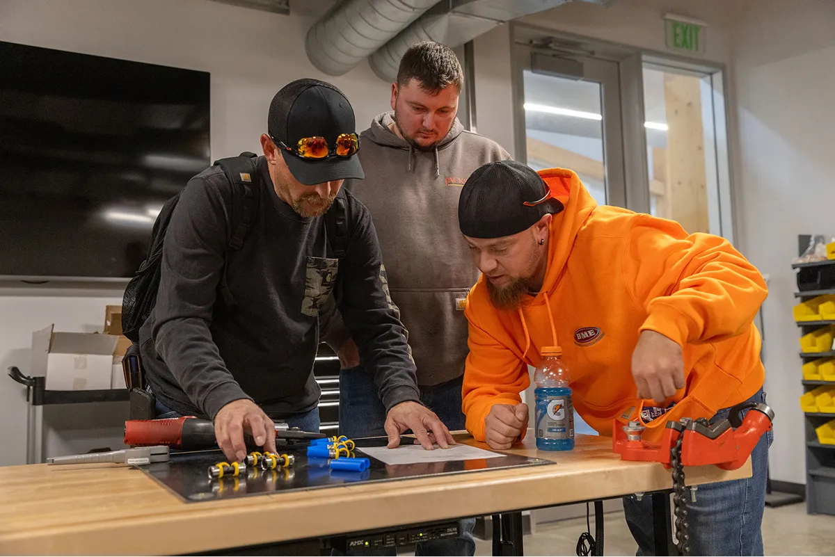 this image shows three workers or apprentices collaborating around a workbench during a hands-on training session