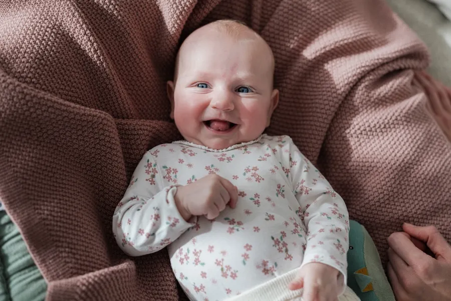 Ein lachendes Baby auf einer rosa Decke.