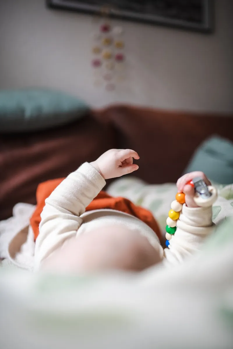 Baby spielt mit Schnullerkette auf dem Sofa.