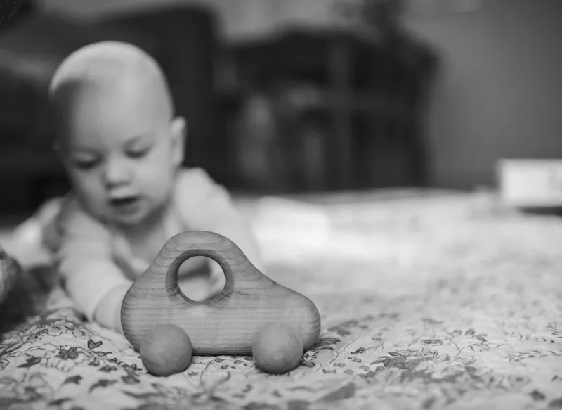 Ein Baby spielt auf einer Krabbeldecke mit einem Holzauto bei einem Familienfotoshooting mit einer Fotografin.
