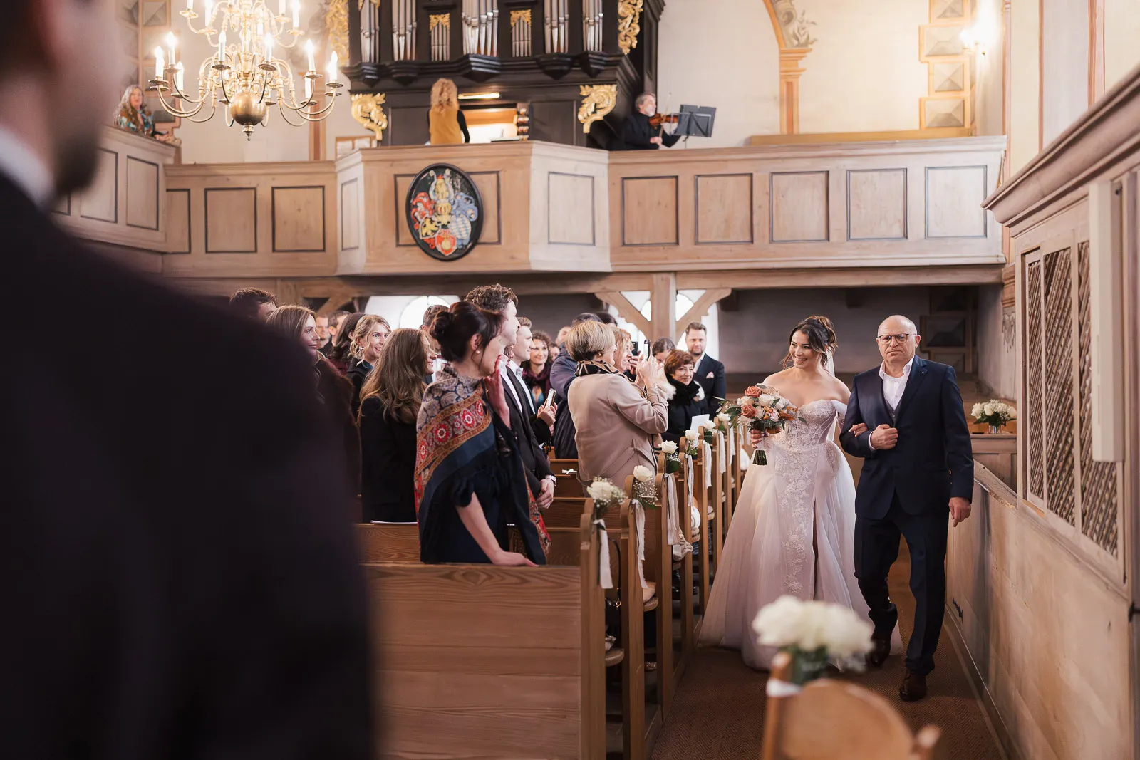 Braut und ihr Vater schreiten in einer Kirche in Grosskarlbach den Gang entlang, Gäste schauen und fotografieren.