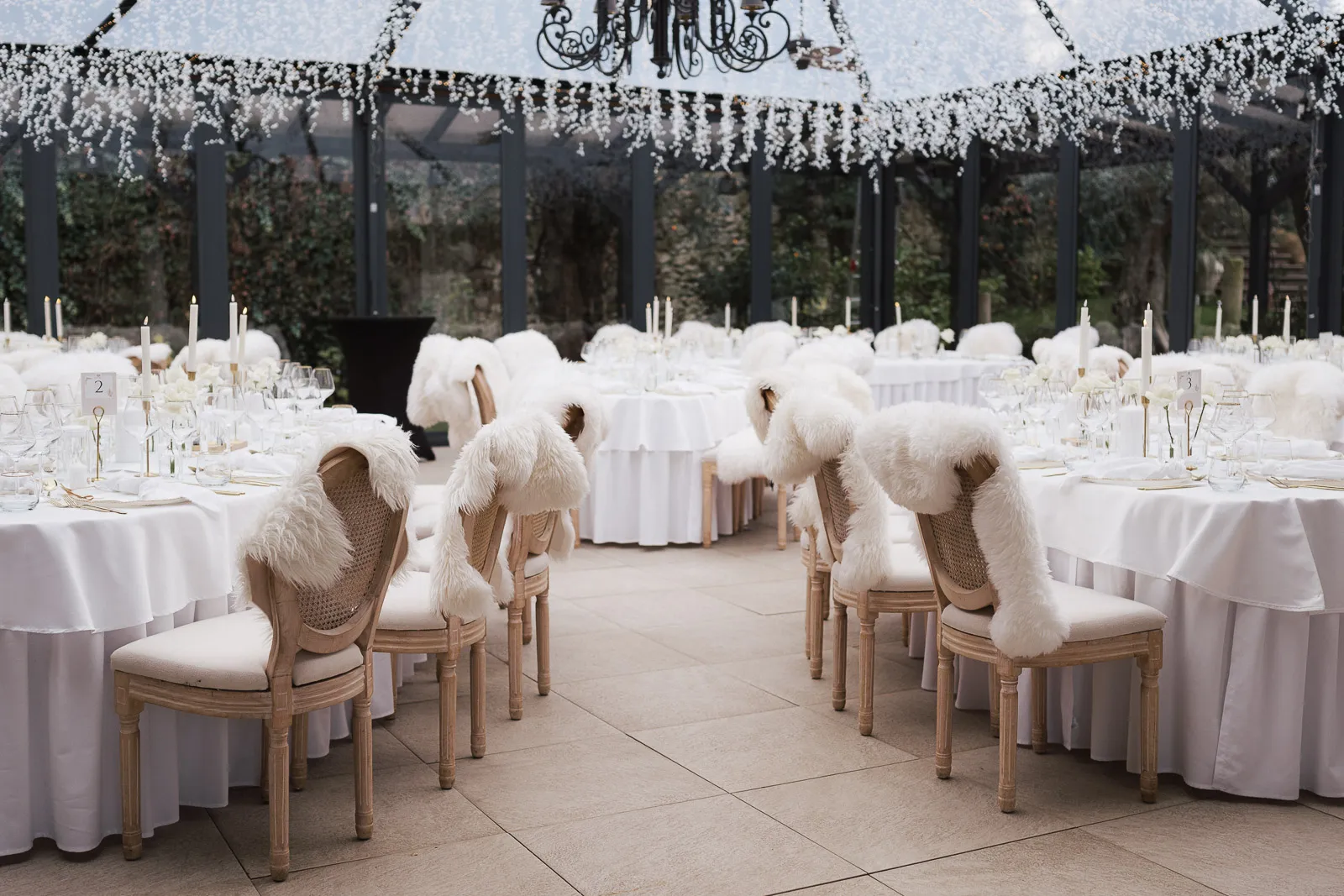 Winterhochzeitstische mit weißen Tischdecken, Kerzen und Stühlen mit weißen Fellüberwürfen.