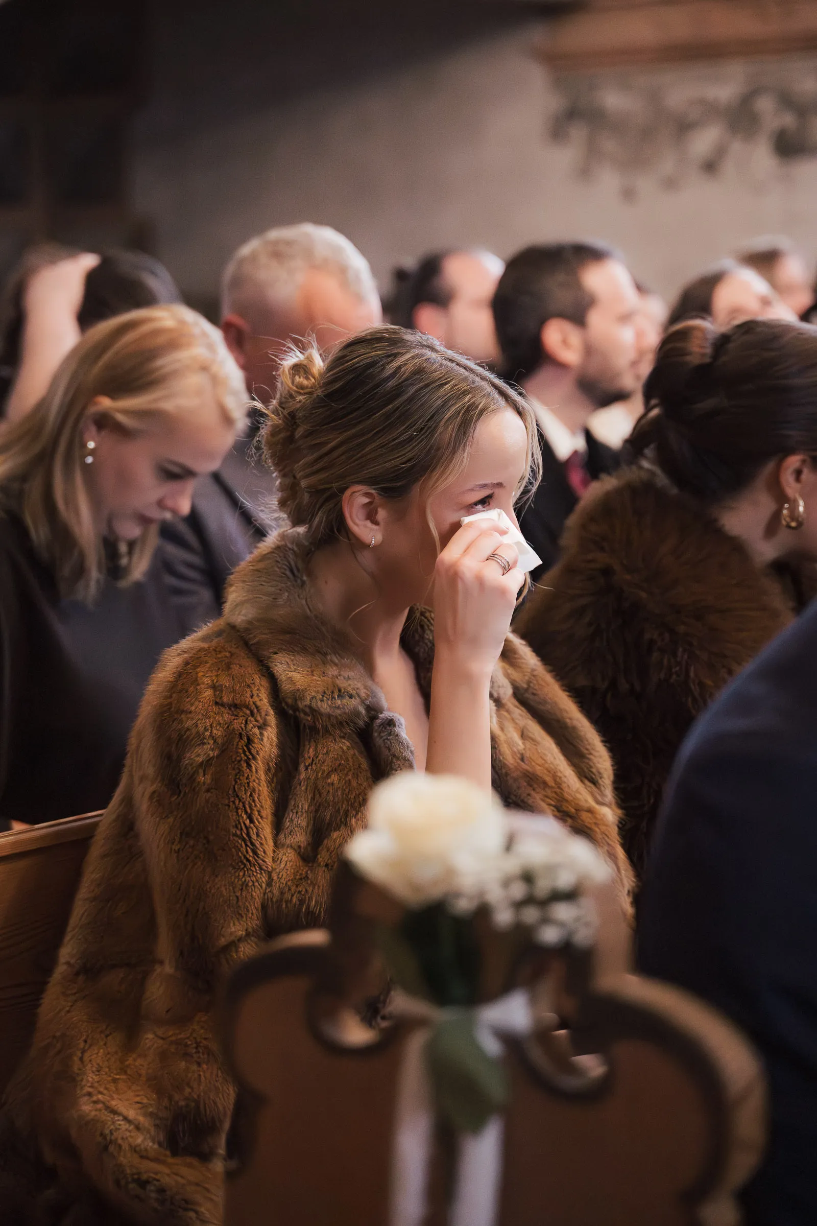 Frau im braunen Pelzmantel wischt sich mit Taschentuch bei einer Hochzeit die Tränen ab.