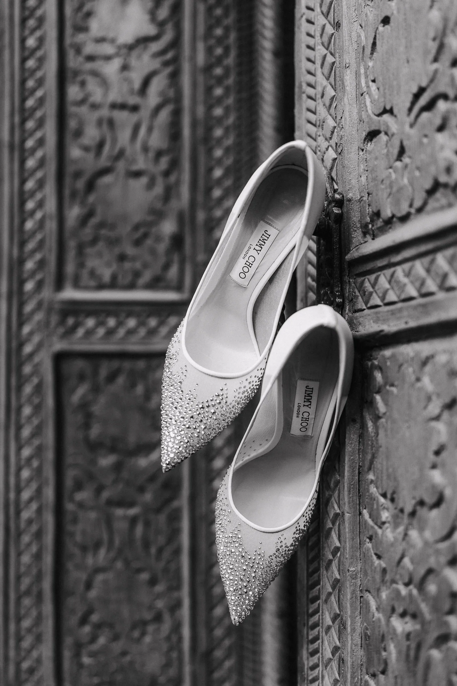 Spitze, mit Strass verzierte Jimmy Choo Damenschuhe hängen an einer verzierten alten Tür.