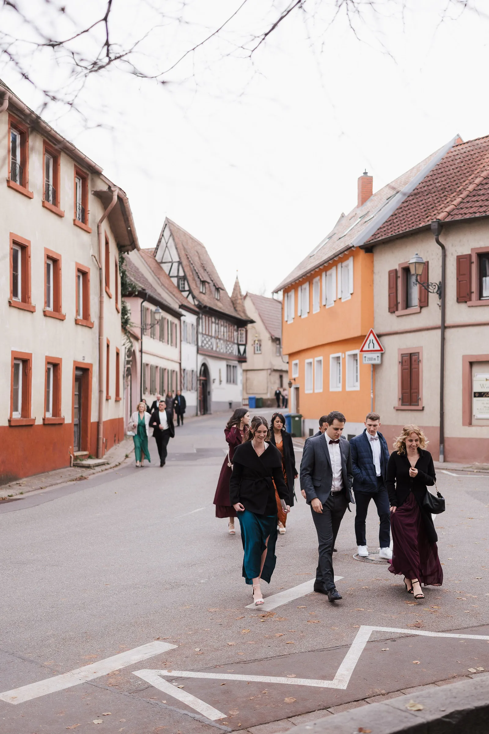 Eine Gruppe festlich gekleideter Personen geht auf einer ruhigen Straße im malerischen Grosskarlbach zur Trauung in die Kirche.