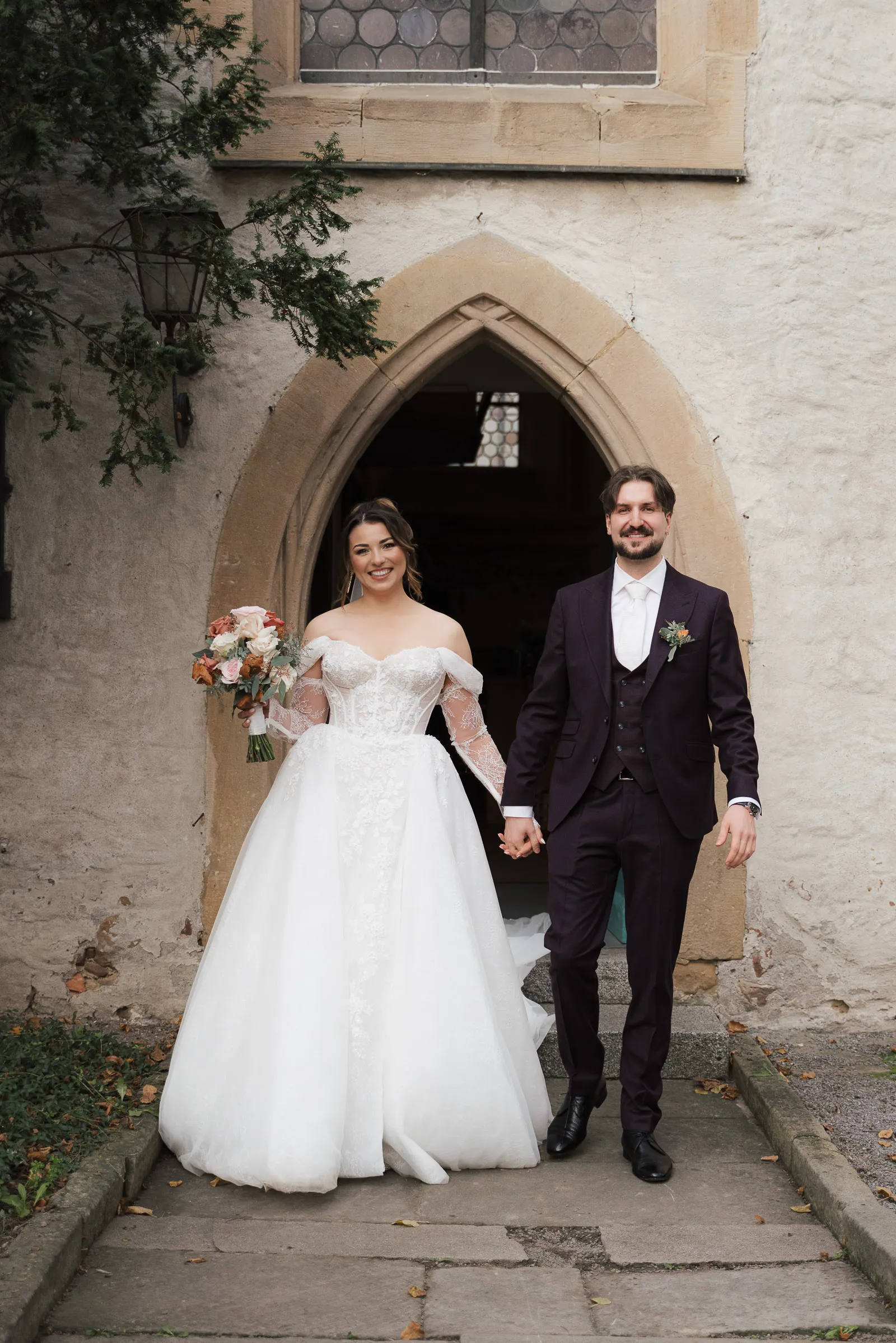 Brautpaar verlässt lachend eine Kirche in Großkarlbach, die Braut hält einen Blumenstrauß, Hand in Hand.