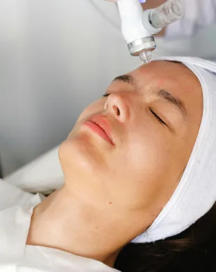 Woman with eyes closed receiving a facial treatment using a handheld device on her forehead.