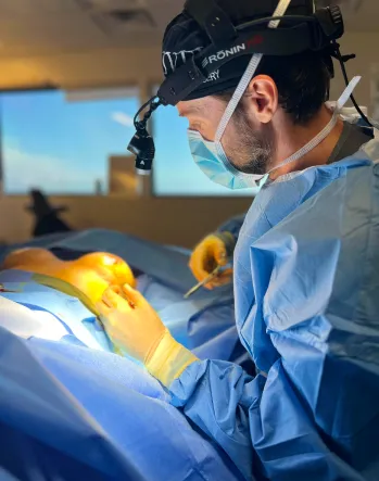 Surgeon wearing a headlamp and mask performing surgery on a patient's leg in an operating room.