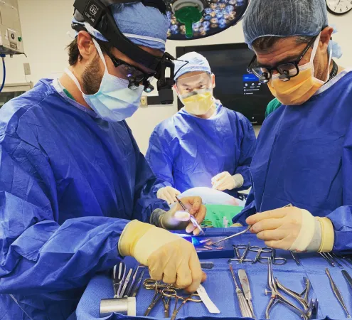 Three surgeons in blue scrubs and surgical masks performing an operation with surgical tools on a tray.