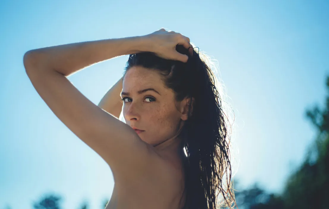 Woman with wet hair pulling it back, looking over her shoulder against a clear blue sky.
