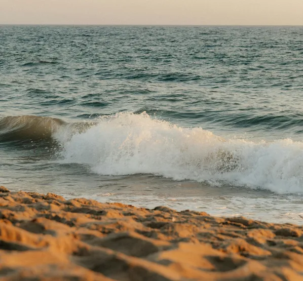 Waves crashing onto a sandy beach under a clear sky during sunset.