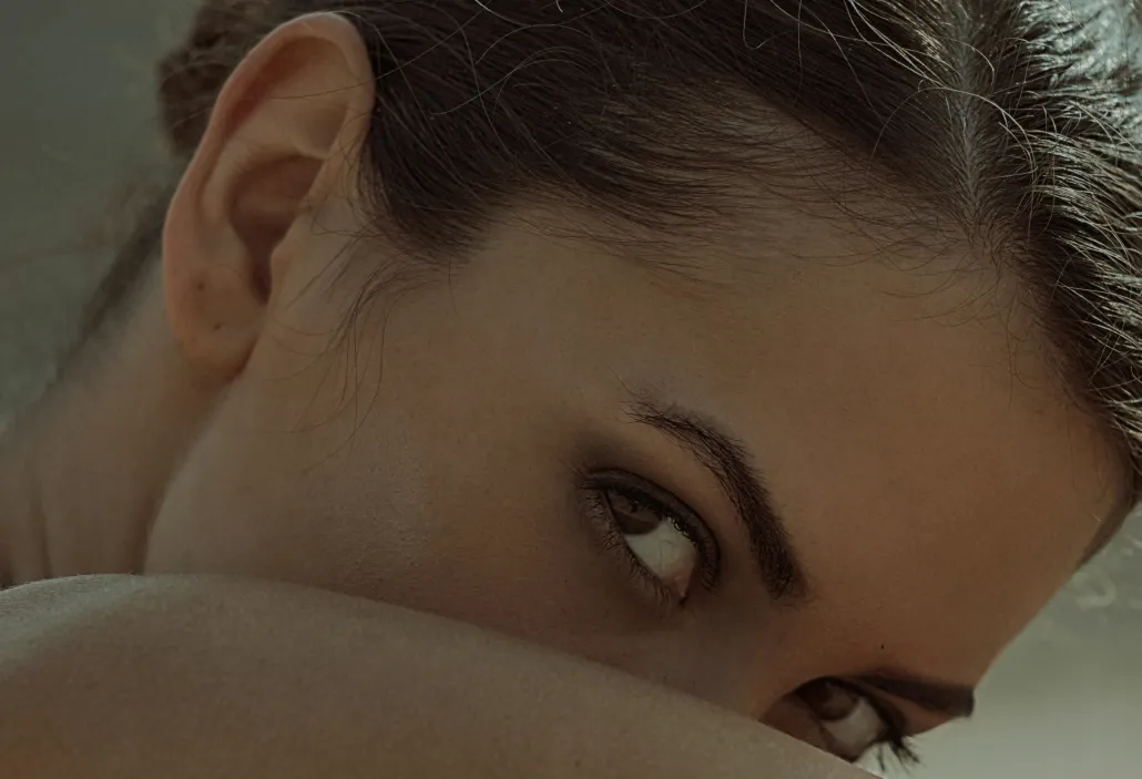 Close-up of a woman with dark hair looking sideways over her shoulder, showing her eyes and part of her ear.