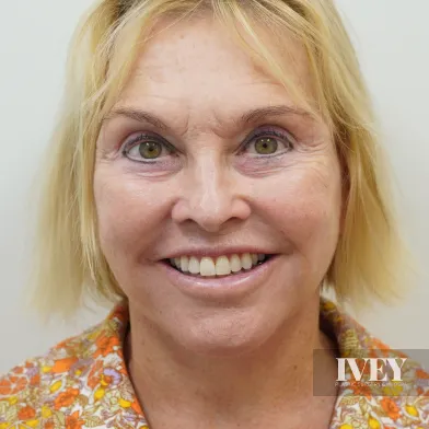 Smiling middle-aged woman with blonde hair wearing a floral-patterned shirt against a light background.