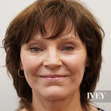 Smiling middle-aged woman with short brown hair and hoop earrings against a plain light background.