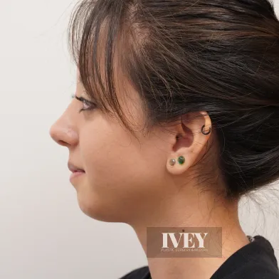 Profile of a woman with dark hair in a bun wearing three earrings along her ear.