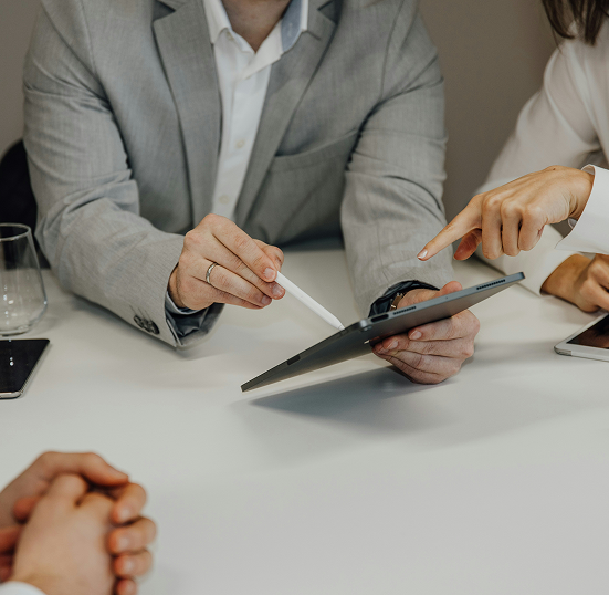 Two people in business attire discussing content on a tablet with a stylus at a white table.