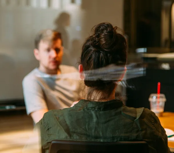 Two people having a conversation in a casual setting, viewed from behind one person's head.
