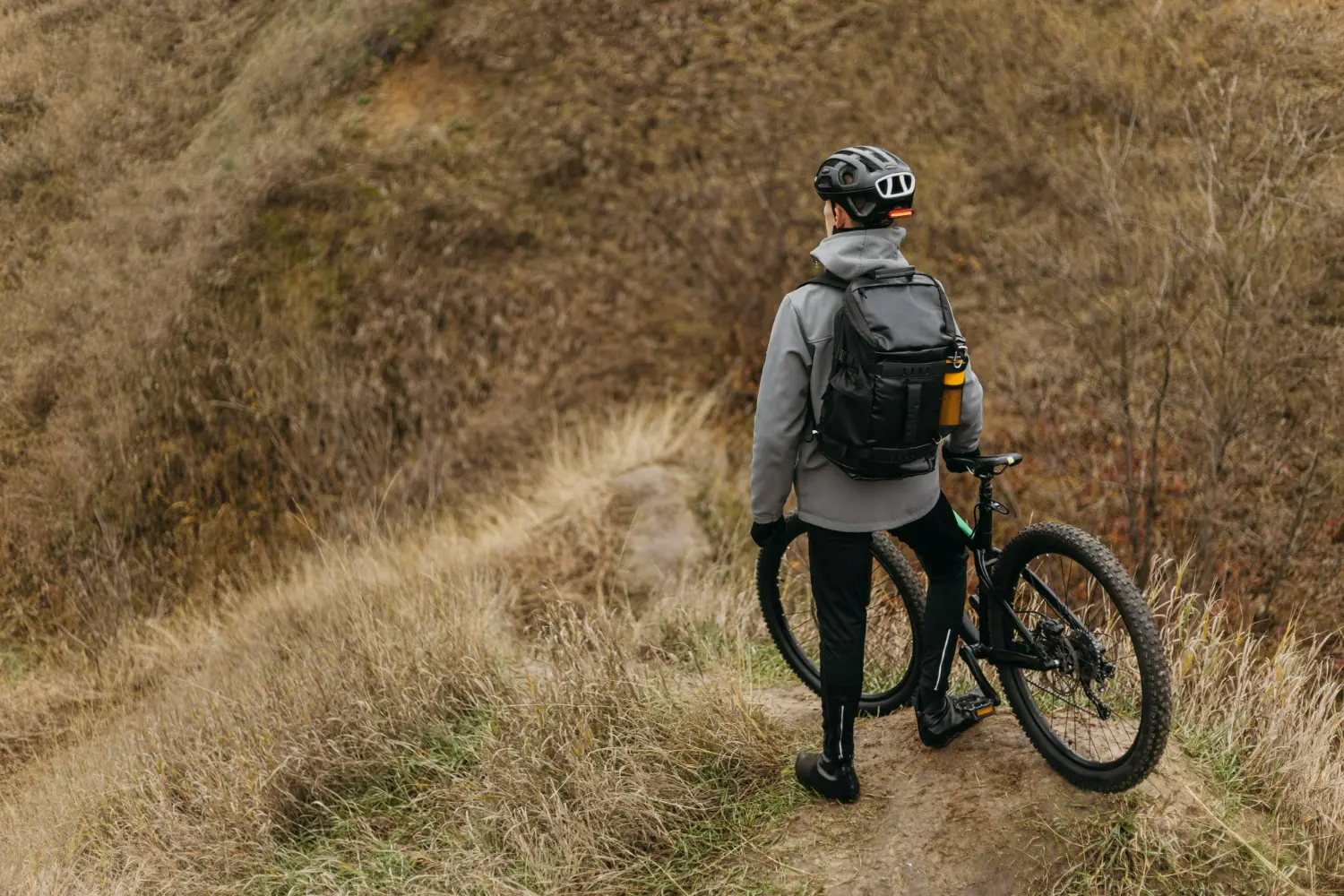 man looking away with holding his bicycle on a hill