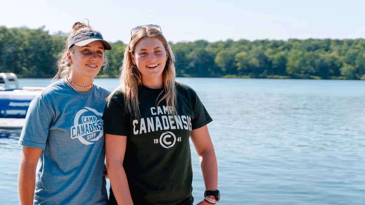 Two summer camp staff laughing near a lake.