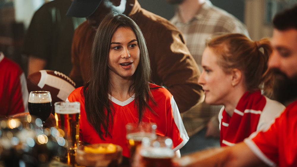 Young sports fans chatting while watching a game at a local bar