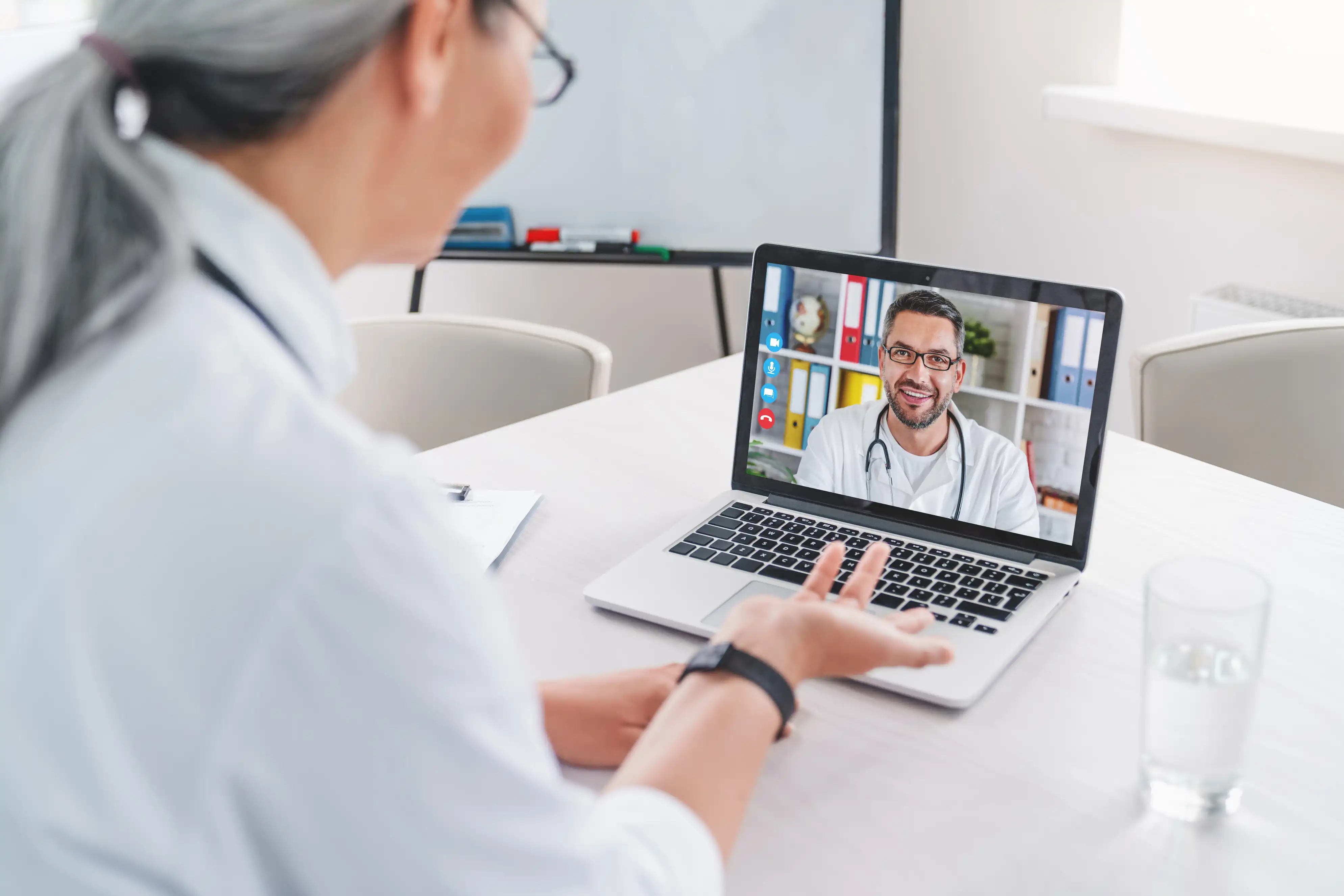 Adult female doctor has video call and chatting with colleague on laptop in clinic. Medical workers teamwork. Briefing about disease, illness treatment